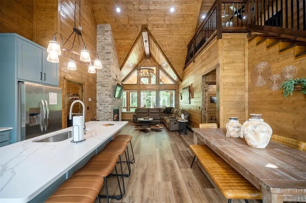 Gilded Spur great room before Yellowwood Atelier design, Broken Bow OK cabin: cathedral ceiling, sage-painted kitchen island, exposed wood walls, generic chandelier, no art or programming