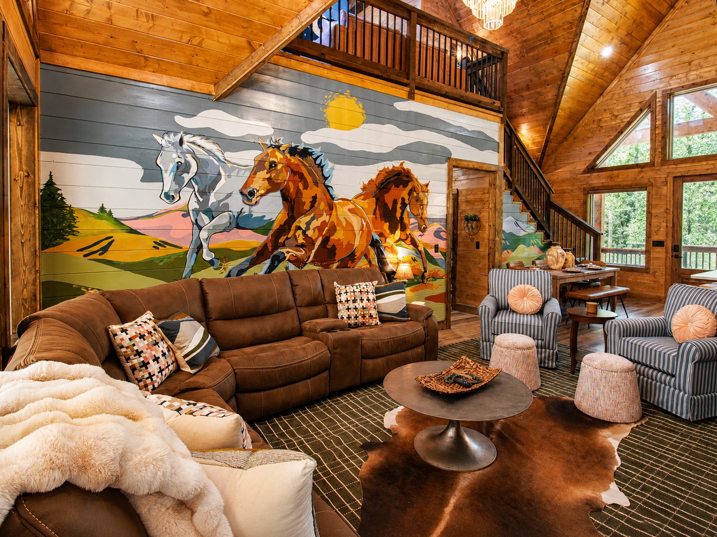 Gilded Spur great room horse mural by Magic Hat Murals (Jes Weiner), Hochatown OK equestrian-luxury cabin: hand-painted horse mural anchoring the wall, cowhide rug, leather sectional, blue-striped armchairs