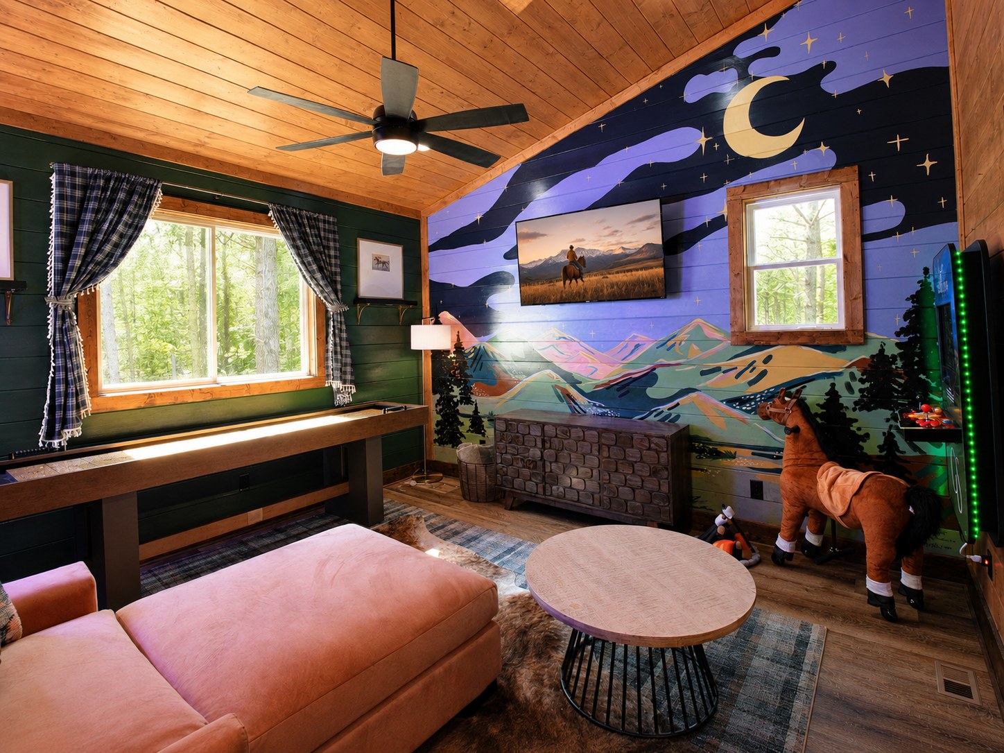 Gilded Spur upstairs loft game lounge after Yellowwood Atelier design, Hochatown OK cabin: 'Spur Up Some Fun' custom neon, shuffleboard table, layered cushion seating, hand-painted slant-wall mural
