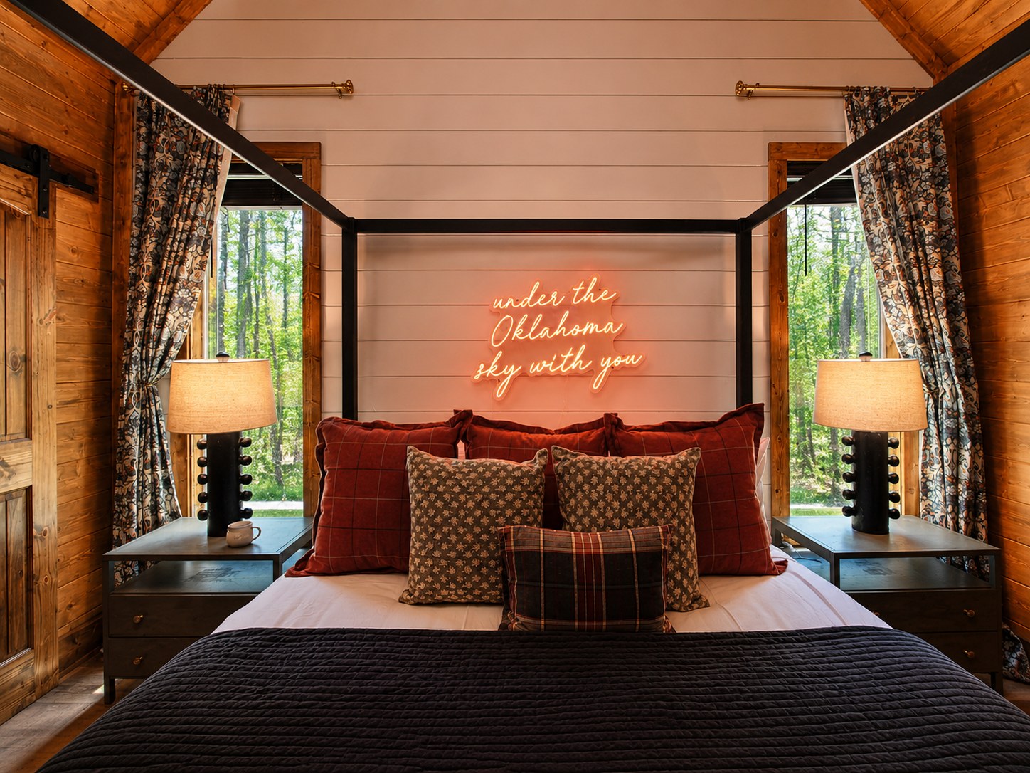 Gilded Spur primary bedroom after Yellowwood Atelier design, Hochatown OK equestrian-luxury cabin: 'under the Oklahoma sky with you' custom neon sign, four-poster steel bed, oxblood velvet bedding, plaid pillows, equestrian-print drapes