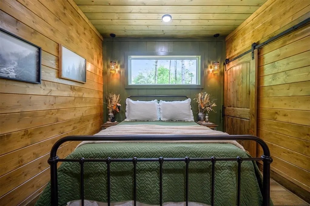 Gilded Spur second bedroom before Yellowwood Atelier design, Broken Bow OK cabin: dark wood walls, basic iron bed, plain bedding, no character