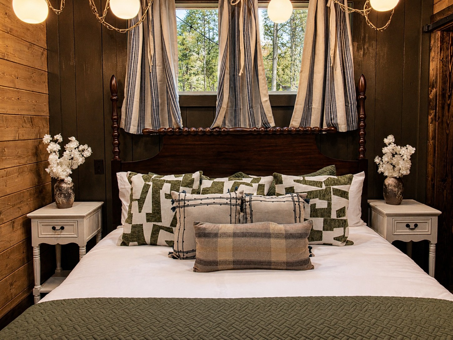 Gilded Spur second bedroom after Yellowwood Atelier design, Hochatown OK vacation rental cabin: layered linens, plaid throw, draped pendant lights, refined equestrian-cabin styling