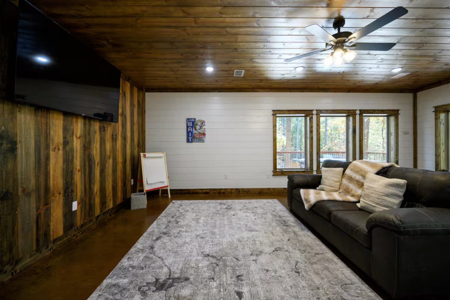 Generic basement game room before — blank shiplap walls, dark sectional, no programming