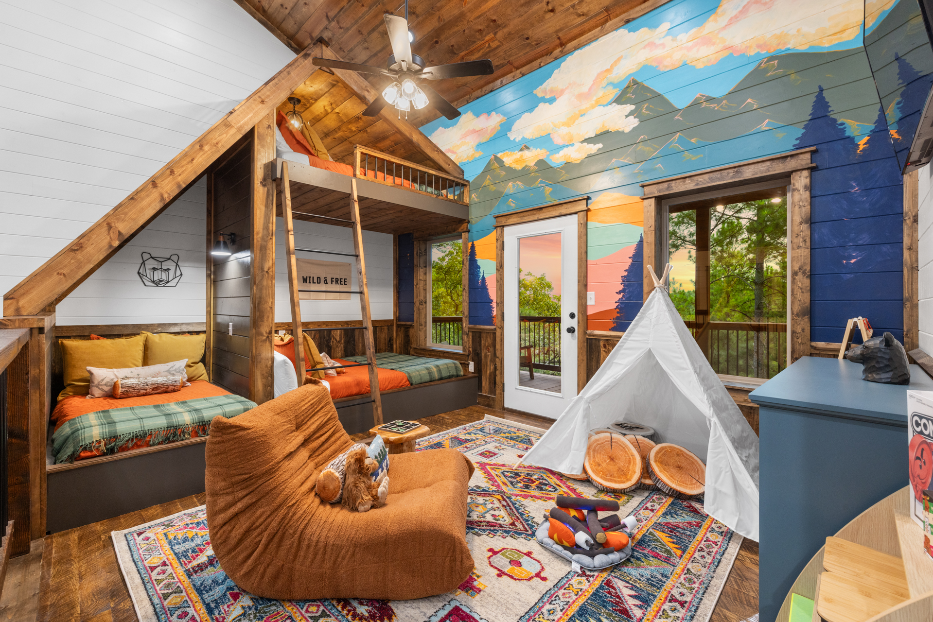 Lazy Lariat bunk room after — custom-built cabin-style bunks, hand-painted mountain mural on the wall, teepee, layered rugs