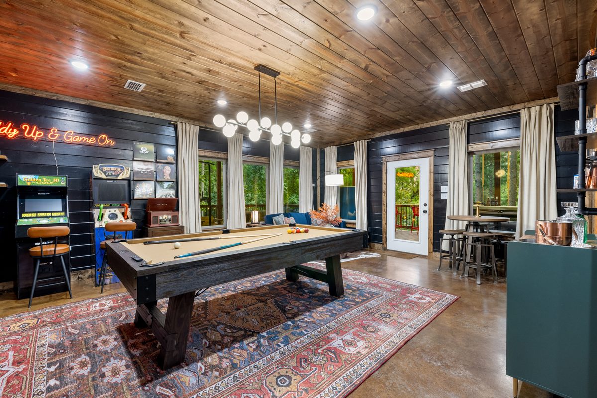 Game room with a pool table, arcade and &lsquo;Giddy Up & Game On&rsquo; neon at Lazy Lariat in Broken Bow, Oklahoma