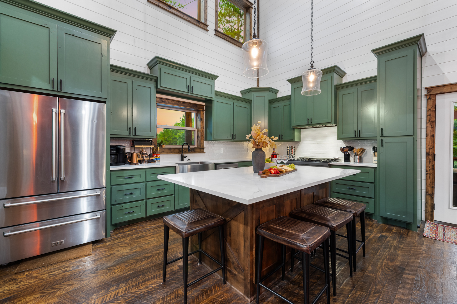 Wide view of the Lazy Lariat kitchen — sage Shaker cabinets, marble island, leather barstools, ZLINE pro-style range, herringbone floor