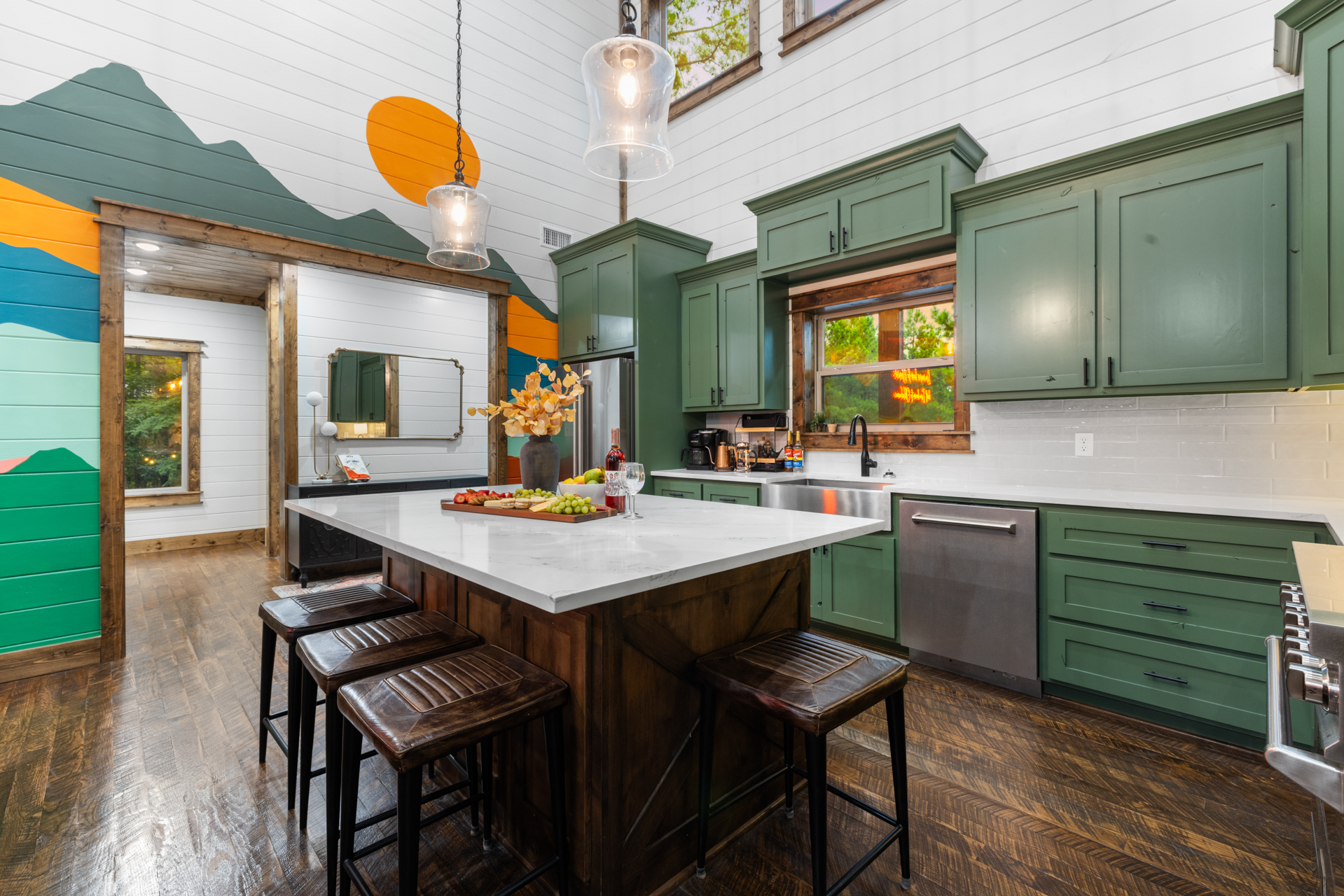 Sage-cabinet kitchen with charcuterie on the marble island, Oklahoma mural visible through the doorway