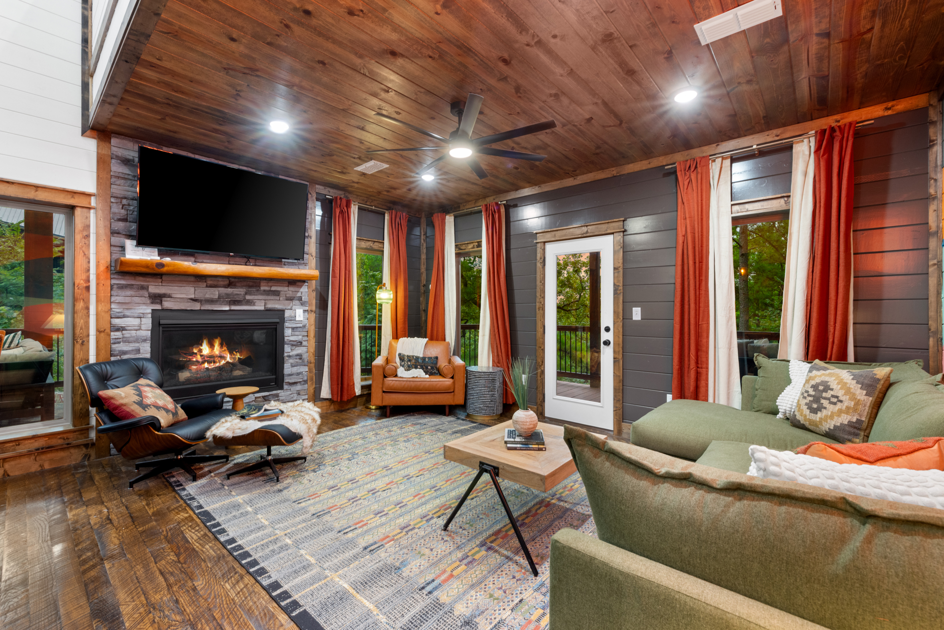 Lazy Lariat living room with stone fireplace, Eames lounger, leather sofa, green sectional, rust velvet curtains, layered Aztec rug