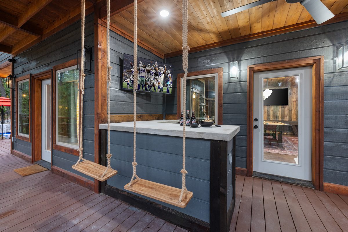 Covered porch bar with rope swings and a game-day TV at Lazy Lariat cabin in Broken Bow, Oklahoma