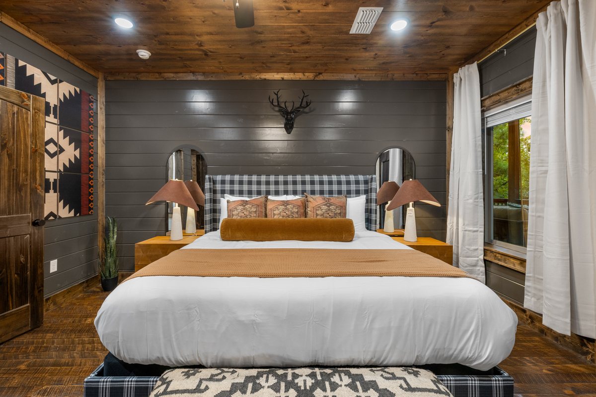 Primary bedroom with a plaid upholstered headboard, mounted antlers and Aztec accents at Lazy Lariat in Broken Bow, Oklahoma